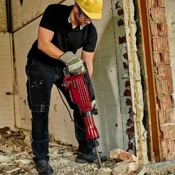 Einhell Martillo demoledor TC-DH 43 - 1.600 W, 43 J, Alojamiento SDS-Hex - Un trabajador de la construcción con casco está usando un martillo demoledor Einhell para demoler una pared.