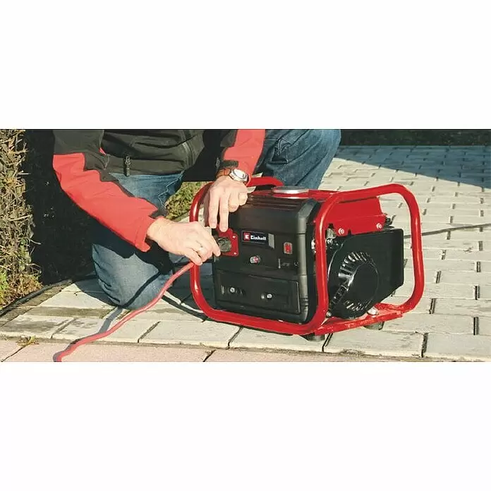 Einhell Generador TC-PG 10/E5 - Potencia nominal: 680 W, Volumen del depósito: 4 l - Persona conectando un cable rojo a un generador rojo y negro sobre adoquines exteriores.