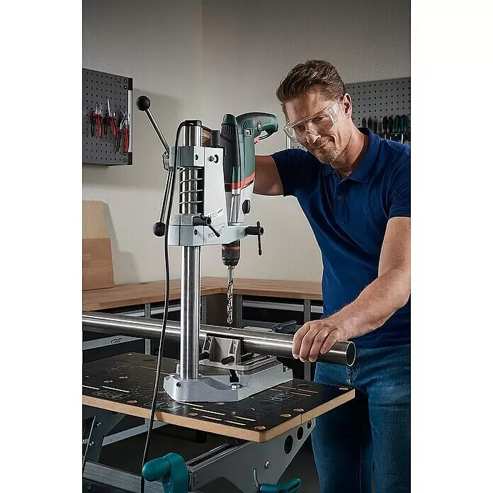 Wolfcraft Metallbohrer - 1 Stk., Durchmesser Bohrer: 3,1 mm, HS-Stahl - Mann mit Schutzbrille bedient grauen Bohrständer mit grüner Bohrmaschine, um ein Loch in ein silbernes Metallrohr zu bohren.
