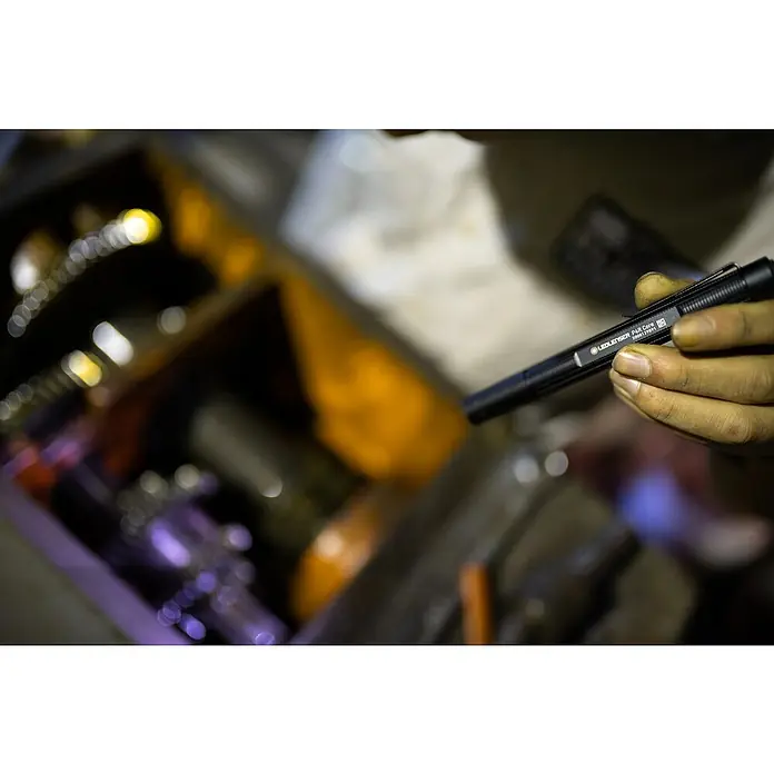 Ledlenser Taschenlampe P4R Core - 15 lm - 200 lm, IP54 - Nahaufnahme einer Ledlenser P4R Core Stiftleuchte, gehalten vor Werkzeugen in einer Werkstatt, ideal für präzise Ausleuchtung.