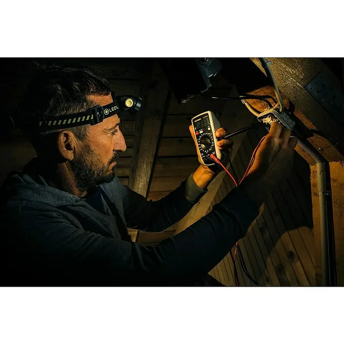 Ledlenser Stirnlampe H5R Work - 15 lm - 500 lm, IP67 - Ein Elektriker mit Stirnlampe prüft mit einem Multimeter eine elektrische Verbindung. Der Fokus liegt auf der Messung.