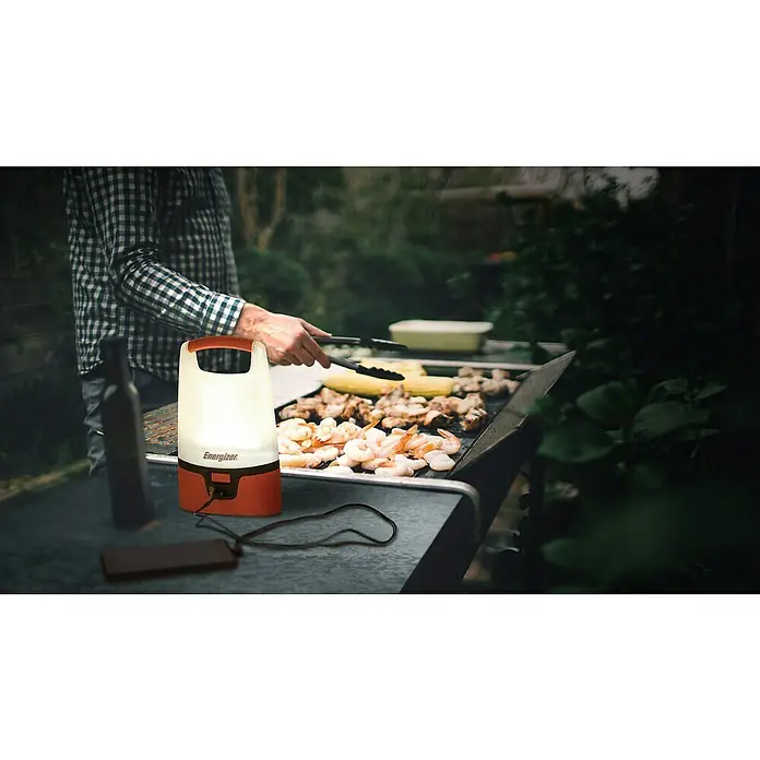 Energizer Lámpara de camping camping recargable - 7 x 17 x 30 cm, 1.000 lm - La linterna Energizer ilumina una parrilla con gambas y maíz mientras una persona usa pinzas. ¡Perfecta para actividades al aire libre!