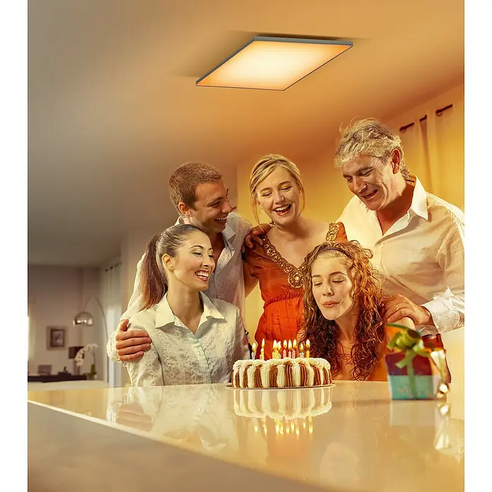Ledvance Smart+ WiFi LED-Panel Planon Frameless - 40 W, L x B x H: 69 x 596 x 596 mm, Weiß - Eine quadratische Deckenleuchte scheint warm über einer Familie, die einen Geburtstag feiert. Das Licht betont die festliche Atmosphäre.