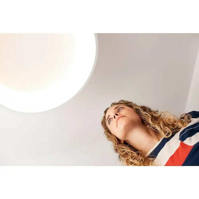 Ledvance Smart+ WiFi LED-Deckenleuchte rund Cylinder24 W, Ø x H: 450 x 134 mm, Weiß - Nahaufnahme einer Frau, die zu einer modernen, runden Deckenleuchte aufblickt, die helles, gleichmäßiges Licht spendet.