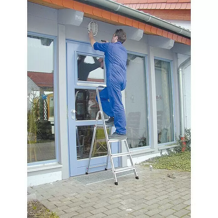 Krause Corda Escalera de tijera - Altura de trabajo: 2,8 m, Número de peldaños: 4 ud., Carga soportada: 150 kg, Aluminio - Hombre en una escalera de tijera plateada, ajustando una lámpara exterior.
