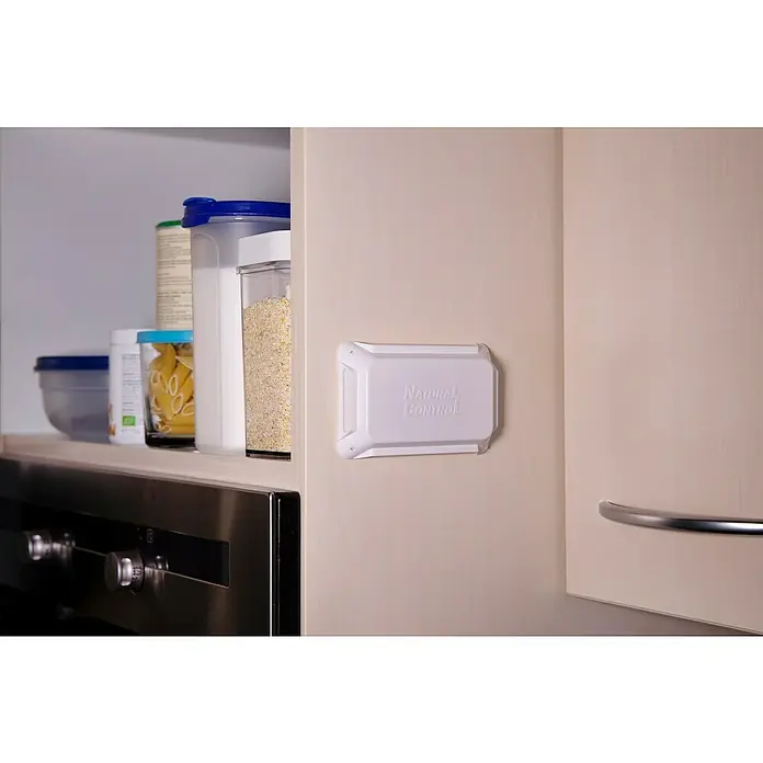 Swissinno Trampa para polillas - 2 ud. - Un producto "Natural Control" está fijado a la pared de un armario de cocina claro, mientras que los suministros son visibles arriba y un horno abajo.