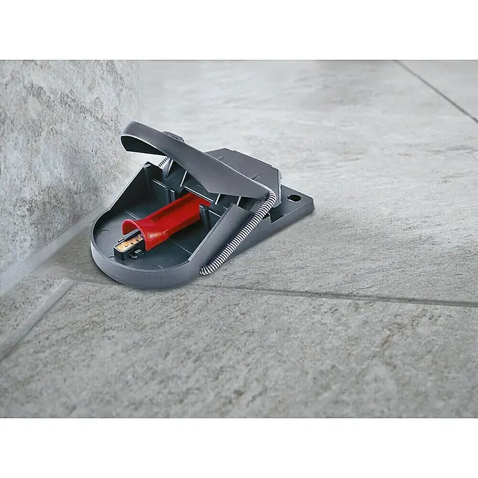Swissinno Mausefalle Supercat Pro - Schlagfalle - Eine graue Schlagfalle mit einem roten Köderbehälter, die auf einem gefliesten Boden neben einer Wand steht.