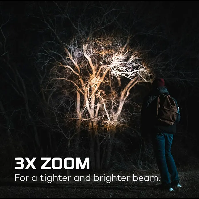 Nebo Tools Linterna táctil Newton - 3,81 x 4,78 x 17,78 cm, 1.000 lm, IP67 - Un hombre está de pie en la oscuridad, iluminando un árbol con una linterna de zoom 3X, enfocando para un haz más estrecho y brillante.
