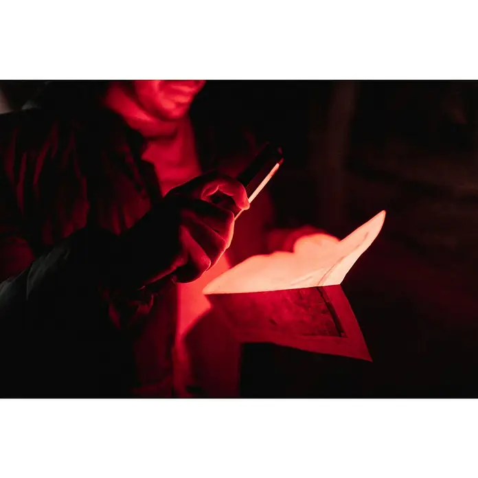 Nebo Tools Linterna Newton - 1,78 x 1,78 x 21,34 cm, 400 lm, IPX4 - Una persona ilumina un sobre abierto con una lámpara brillante, haciendo que el contenido brille en rojo.
