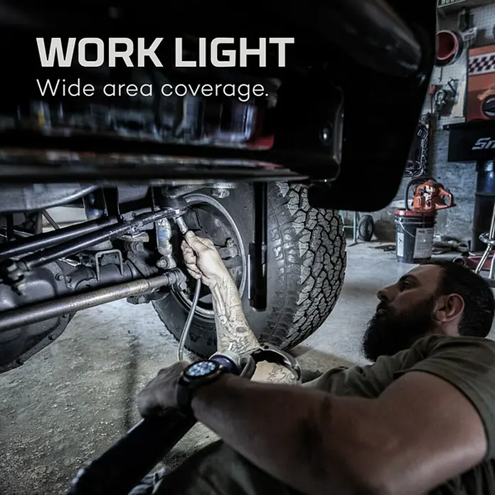 Nebo Tools Linterna Newton - 1,78 x 1,78 x 21,34 cm, 400 lm, IPX4 - Un hombre usa una luz de trabajo mientras repara un vehículo, mostrando la amplia cobertura del área de la lámpara para trabajos detallados.