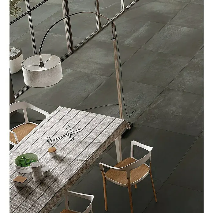 Feinsteinzeugfliese Metallo Ferro - 60 x 60 cm, Schwarz, Matt - Elegantes Interieur mit Esstisch, Stühlen und einer stilvollen Stehlampe, alles auf einem modernen, grauen Fliesenboden.
