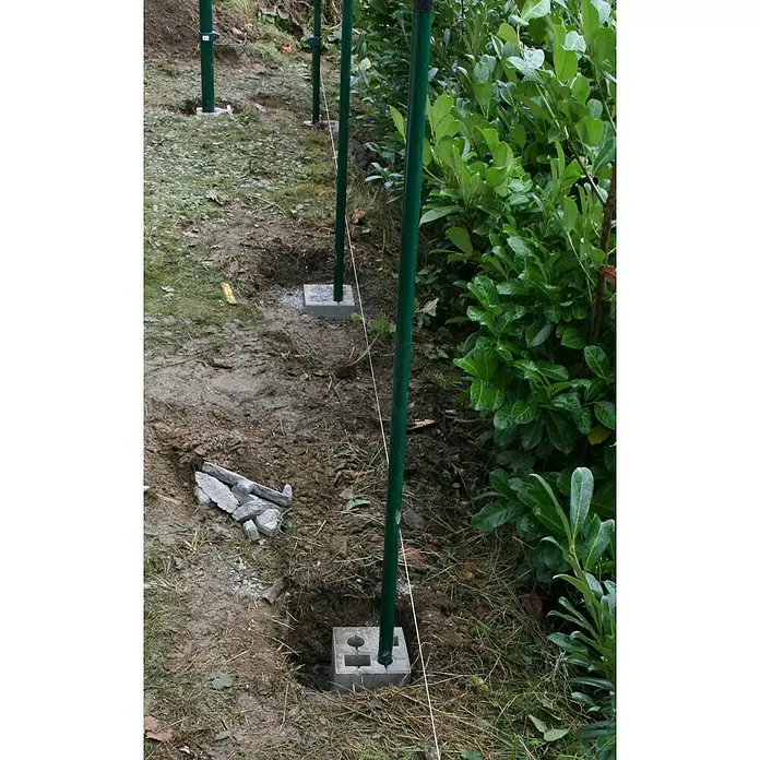 Christoph Zaun-Fundamentstein 4in1 - Grau, 19 x 19 x 25 cm, Beton - Das Bild zeigt eine Reihe von grünen Zaunpfosten, die in Betonfundamente eingesetzt sind, wobei eine Richtschnur die Ausrichtung der Pfosten vorgibt.