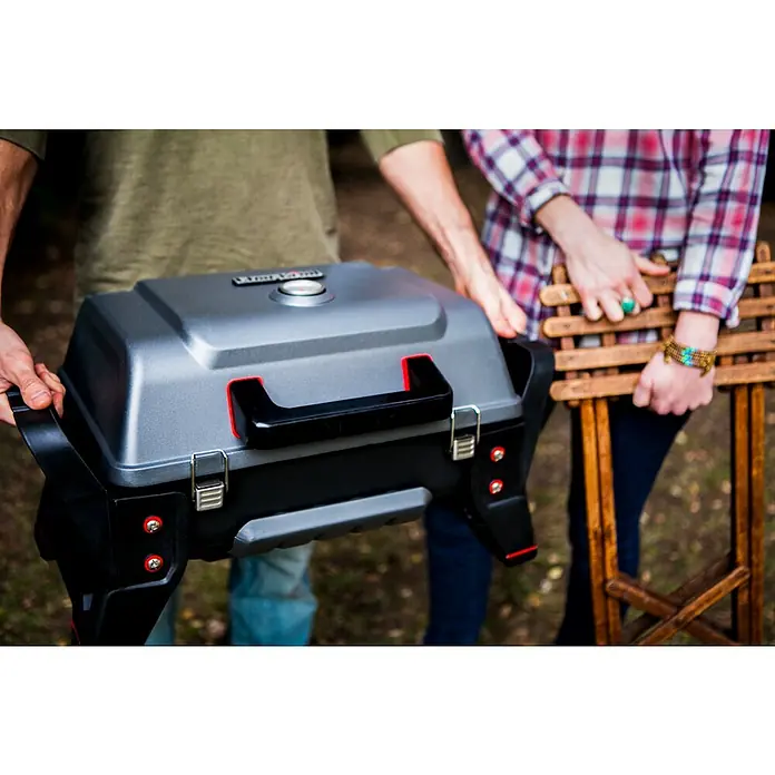 Char-Broil Gasgrill Grill2Go - Grillfläche (B x T): 44 x 28 cm, 2,7 kW, Anzahl Brenner: 2 - Zwei Personen tragen einen tragbaren Holzkohlegrill mit grauem Deckel und schwarzen Akzenten sowie einen Holzstuhl.