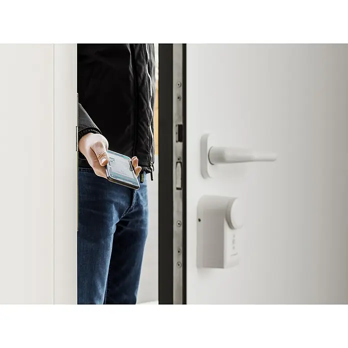 Homematic IP Set Türschlossantrieb mit Keypad & Access Point 2 - L x B x H: 36 x 56 x 118 mm, Weiß - Person, die ein Smartphone zum Entsperren eines smarten Türschlosses verwendet.