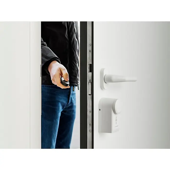 Homematic IP Funkfernbedienung HmIP-KRCK - Passend für: Homematic IP Türschlossantrieb, Schwarz, 75 x 38 x 14 mm - Ein Mann, der durch eine Tür geht, die mit einem modernen elektronischen Schloss mit einem Drehknopf ausgestattet ist.