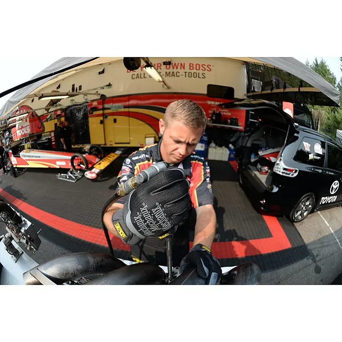Mechanix Wear Arbeitshandschuhe FastFit - L, Schwarz - Ein Mechaniker arbeitet mit Werkzeugen in der Hand, im Hintergrund ein Werkstattwagen und ein Rennwagen.