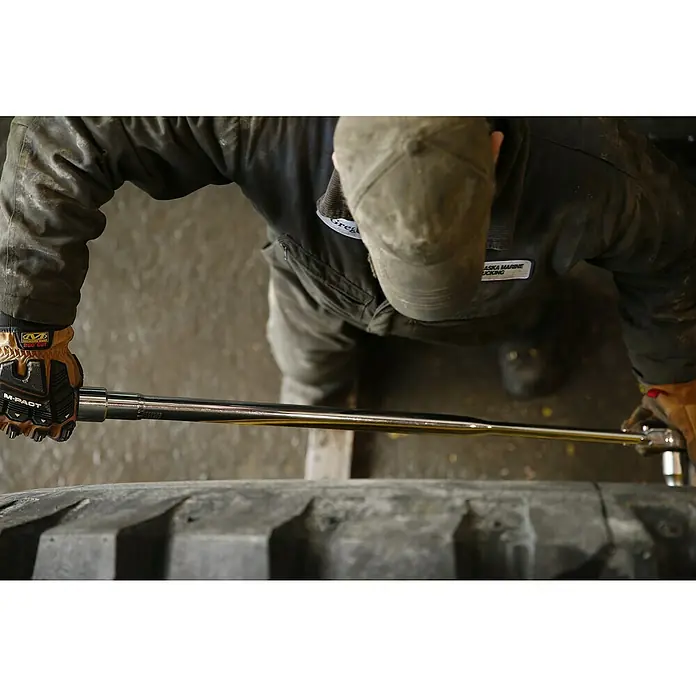 Mechanix Wear Arbeitshandschuhe DuraHide M-Pact Driver F9-360 - S, Braun/Schwarz - Ein Arbeiter mit Handschuhen hantiert mit einem Drehmomentschlüssel an einem großen Reifen. Das Werkzeug ist zentrales Element des Bildes.