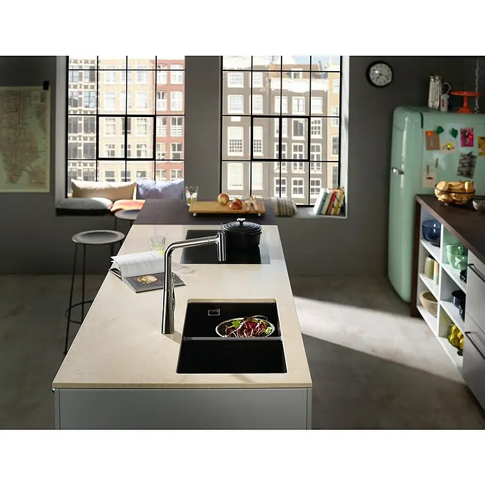 Hansgrohe Fregadero encastrable S510 - U770 2S - 45 x 82 cm, Piedra natural, Número de cubetas: 2 ud., Gris, Resplandeciente - Fregadero de cocina con grifo frente a una ventana con vistas a una ciudad. El fregadero es negro y contiene ensalada. Una cocina elegante.