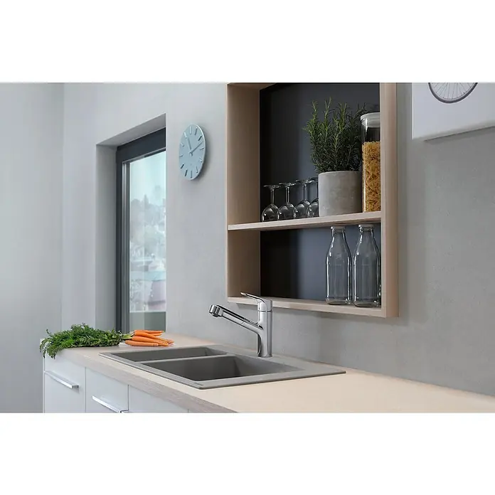 Hansgrohe Grifo de cocina Focus M43 - Cromo, Brillante - Primer plano de un fregadero de cocina moderno con grifo, rodeado de zanahorias frescas y hierbas, bajo un estante elegante.