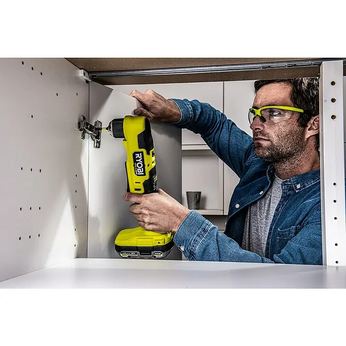 Ryobi ONE+HP Maschinenpaket - Akku-Winkelbohrschrauber RAD18C-0 + gratis Starter-Kit - Ein Mann montiert mit einem gelben Ryobi Akku-Bohrschrauber ein Scharnier an einem weißen Schrank. Er trägt eine Schutzbrille.