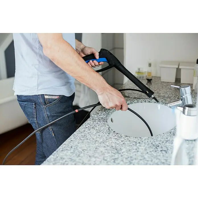 Nilfisk Juego para limpieza de tuberías - Largo: 8 m, Específico para: Limpiadoras de alta presión Nilfisk - El hombre está utilizando un limpiador de vapor para limpiar el lavabo del baño, asegurando un espacio higiénico.