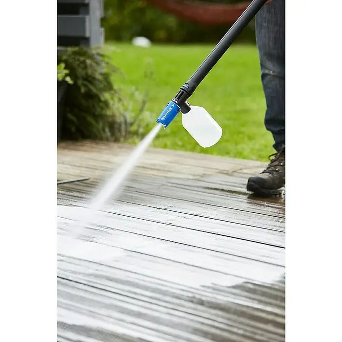 Nilfisk Detergente para madera Stone & Wood Cleaner - 2,5 l - Una hidrolimpiadora con un accesorio de limpieza rocía agua sobre una terraza de madera. La terraza se está limpiando mientras una persona opera la máquina.