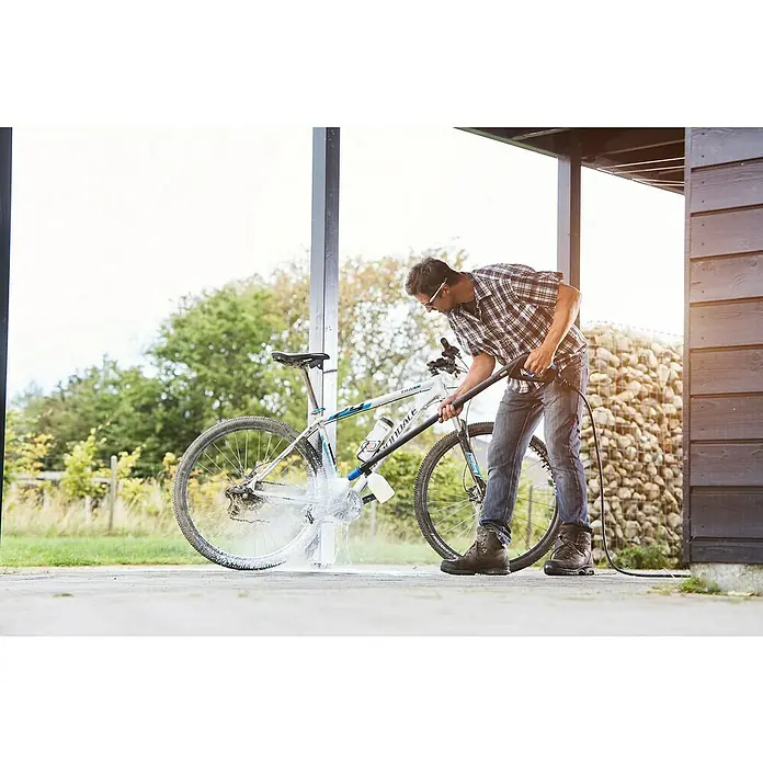 Nilfisk Productos de limpieza Bike & Motorcycle Cleaner - 2,5 l - Un hombre limpia una bicicleta con una hidrolavadora bajo un refugio, eliminando la suciedad para mantenerla limpia.