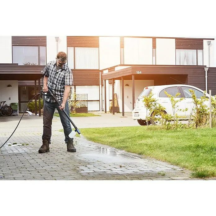 Nilfisk Productos de limpieza Stone Sealer - 2,5 l - Un hombre limpia una acera con una hidrolimpiadora frente a una casa moderna, enfatizando la eficacia del aparato.