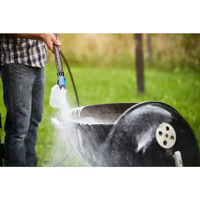 Nilfisk Productos de limpieza Grill & Metal Cleaner - 2,5 l - Una persona limpiando una parrilla con una hidrolavadora. El enfoque está en el proceso de limpieza de la parrilla al aire libre.