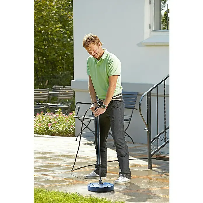 Nilfisk Accesorio de limpieza para suelos exteriores Compact Patio - Específico para: Limpiadoras de alta presión Nilfisk - Un hombre usa un cepillo de limpieza de patios para limpiar un patio de piedra. El piso está mojado y el cepillo rocía agua.