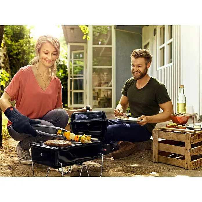 Weber Go-Anywhere Gasgrill - Grillfläche (B x T): 42 x 26 cm, 1,9 kW, Anzahl Brenner: 1 - Ein Paar grillt auf einem tragbaren Grill im Freien, während einer das Essen genießt.