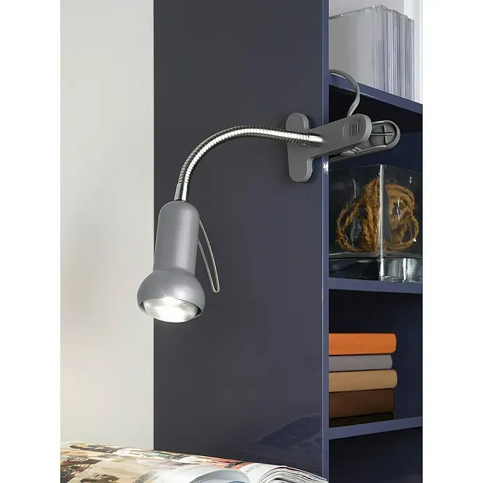 Eglo Klemmleuchte Fabio - 40 W, Farbe Gehäuse: Silber - Nahaufnahme einer grauen Klemmleuchte, die an einem blauen Regal befestigt ist und ein Buch darunter beleuchtet.