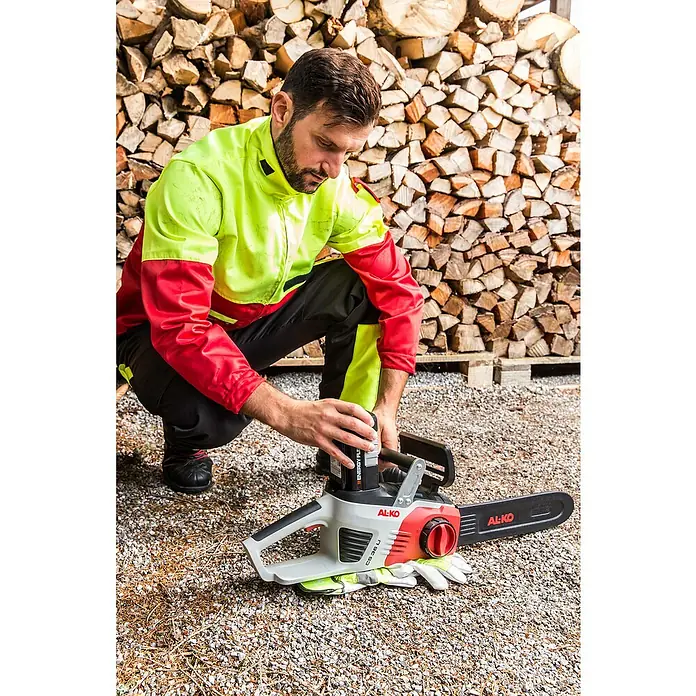 AL-KO 36V Akku-Kettensäge CS 4030 - 36 V, Li-Ionen, Ohne Akku, Schwertlänge: 30 cm - Mann bereitet die AL-KO Akku-Kettensäge CS 36 Li für die Arbeit vor, mit einem Holzstapel im Hintergrund.