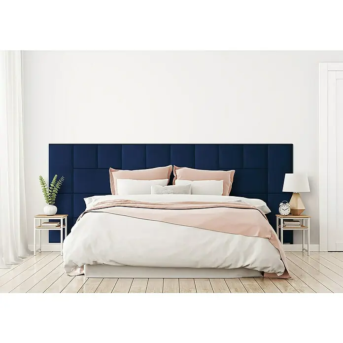 Fllow Wandpolster-Set Velvet A2 - 300 x 120 cm, Blau - Ein Schlafzimmer mit einem marineblauen Stoffkopfteil mit quadratischen Feldern. Die Bettwäsche ist in Weiß- und Rosatönen gehalten.