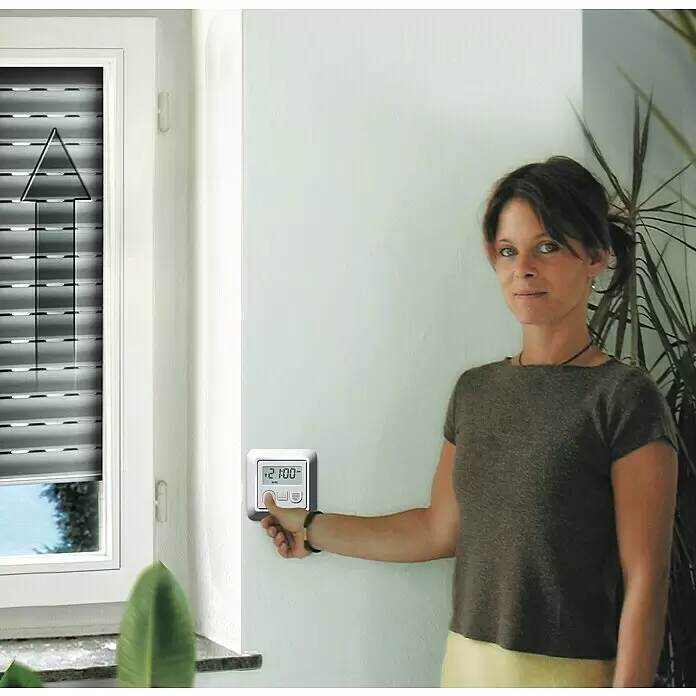 Schellenberg Motor tubular Maxi Standard - Superficie de persiana enrollable máx.: 6,2 m² para persianas de plástico, Longitud de instalación: 500 mm, Fuerza de tracción: 25 kg - Panel de control blanco montado en la pared con pantalla digital '21:00', operado por una mujer para controlar una persiana.