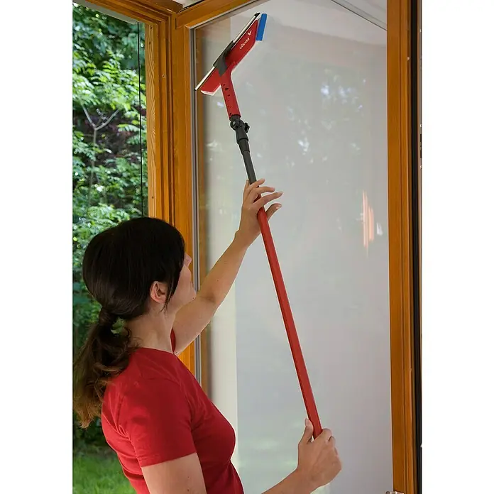 Vileda Fenster-Wischer Profi-Teleskop - Polypropylen, Mikrofaser, 75 cm - 130 cm - Eine Frau benutzt einen Vileda-Fensterwischer mit Teleskopstiel, um Fenster zu putzen. Der rote Stiel ist verlängerbar, ideal für schwer erreichbare Stellen.