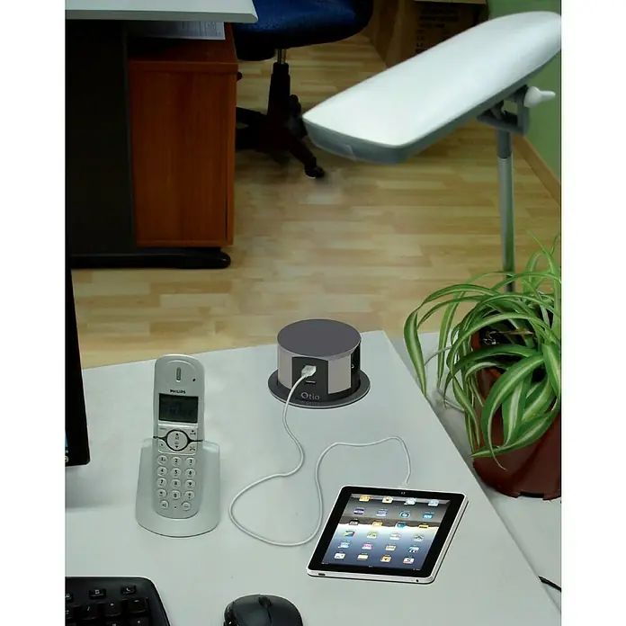 Steckdosensäule - Kunststoff - Das Bild zeigt einen OTIO-USB-Hub, der ein Tablet auflädt, zusammen mit einem Philips-Telefon, einer Maus und einer Tastatur auf einem Schreibtisch.