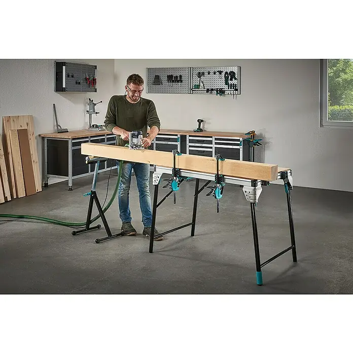 Wolfcraft Werkbank Master Work 1600 - L x B: 76,5 x 110 cm, Arbeitshöhe: 86,3 cm, Belastbarkeit: 120 kg - Ein Mann benutzt einen Router an einem langen Holzstück, das auf einer Wolfcraft Master Werkbank mit Klemmen befestigt ist.\n