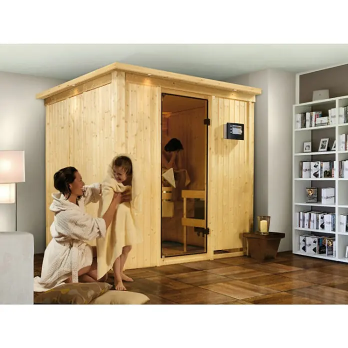 Karibu Elementsauna Sodin - Ohne Ofen, Mit Dachkranz und Beleuchtung, L x B x H: 210 x 184 x 192 cm - Ein entspannender Moment in der Sauna: Mutter trocknet Kind ab, während eine andere Person in der holzvertäfelten Sauna sitzt.