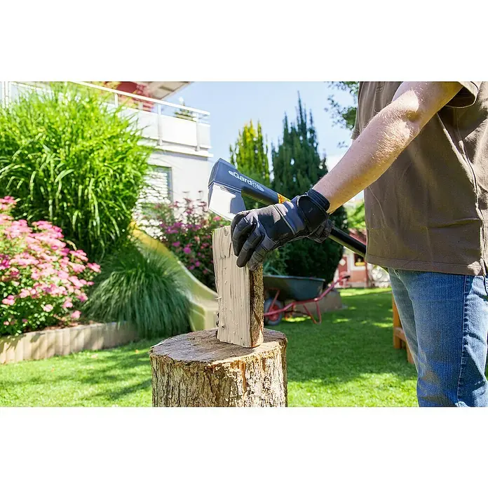 Gardol Profilinie Universalaxt - Länge: 73 cm - Ein Mann spaltet Holz mit einer Gardena Axt, während er Schutzhandschuhe trägt. Im Hintergrund sind ein gepflegter Garten und ein Haus zu sehen.