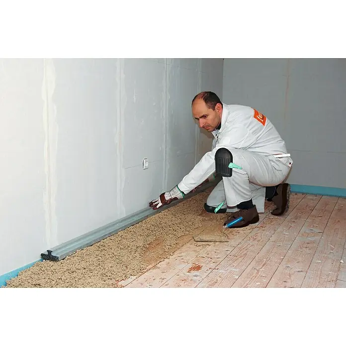 Fermacell Gebundene Schüttung - 80 l - Ein Handwerker kniet und glättet mit einer Richtlatte Dämmmaterial auf einem Holzboden.