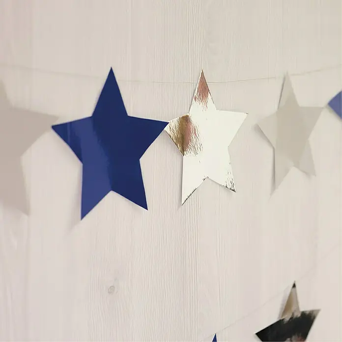 D-c-fix Klebefolie Uni Lack - 200 x 45 cm, Royal Blau, Selbstklebend - Nahaufnahme einer Girlande mit blauen und silbernen Papiersternen, die an einer Wand aufgehängt ist und eine festliche Dekoration darstellt.