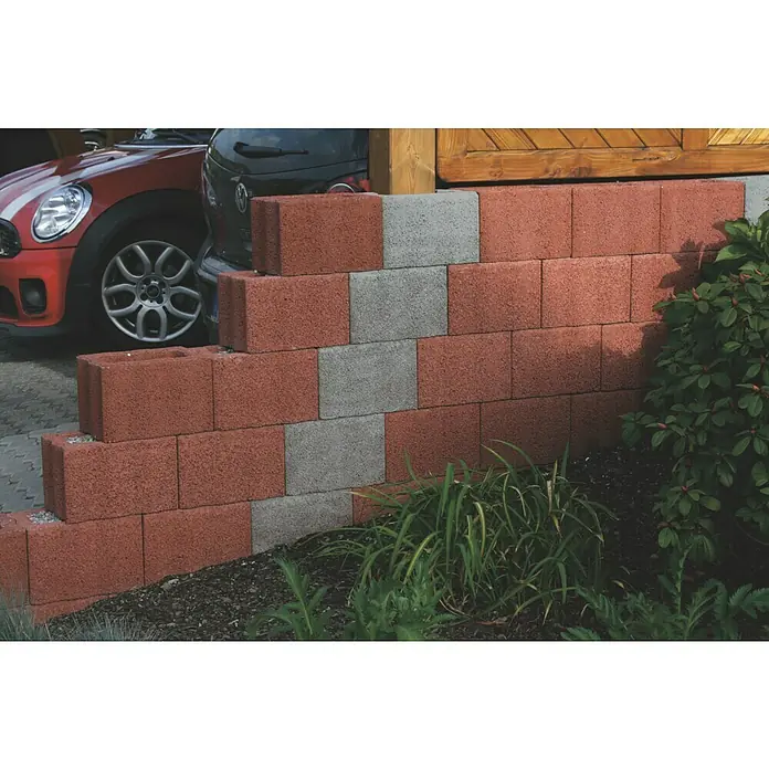 Christoph Pflanzstein Rasterstein - Toskana, 30 x 20 x 20 cm, Beton - Eine rote und graue Betonsteinmauer stützt einen Hang im Garten und verleiht ihm Struktur und Halt. Sie ist dekorativ und funktionell.