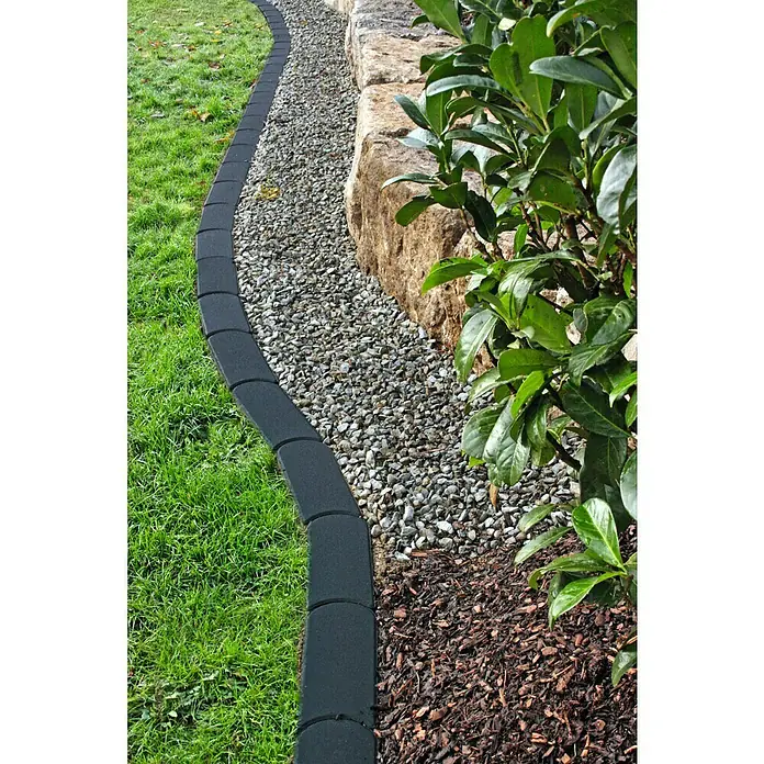 Christoph MähsteinAnthrazit, 22 x 10 x 4,2 cm, Beton - Detailaufnahme einer Rasenkante aus robustem, schwarzem Kunststoff, die einen gepflegten Übergang zu einem Kiesweg schafft.