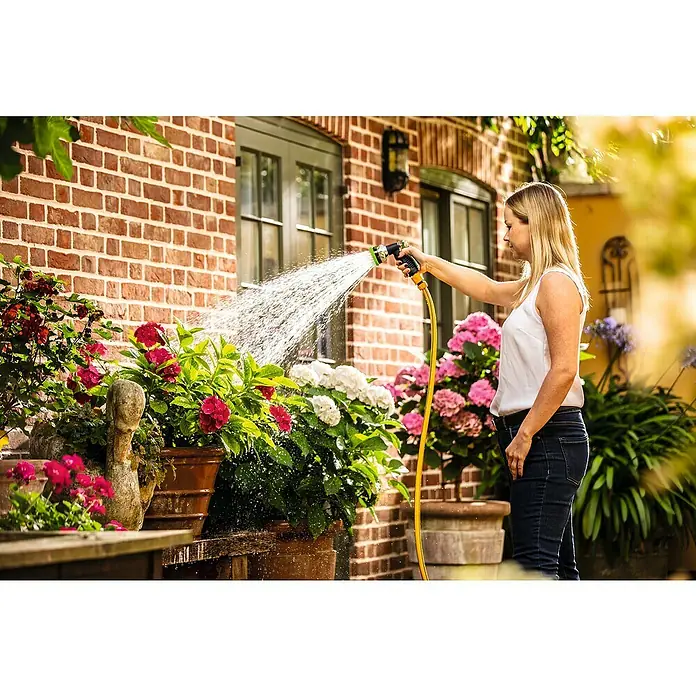 Bosch Power for All 18V Akku-Regenfasspumpe GardenPump 18V-2000 - 18 V, Ohne Akku, Max. Fördermenge: 2.000 l/h - Eine Frau gießt Blumen mit einem gelben Wasserschlauch und einem Sprühkopfaufsatz vor einem Backsteingebäude.