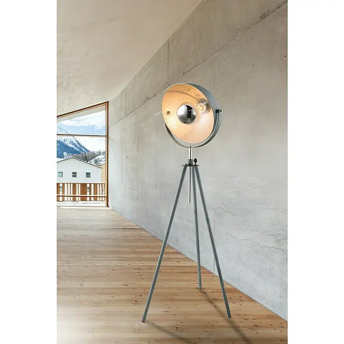 Globo Miram Stehleuchte - Höhe: 179 cm - Eine silberne Stehlampe mit einem runden Lampenschirm steht in einem modern eingerichteten Raum mit Holzboden und Betonwänden.