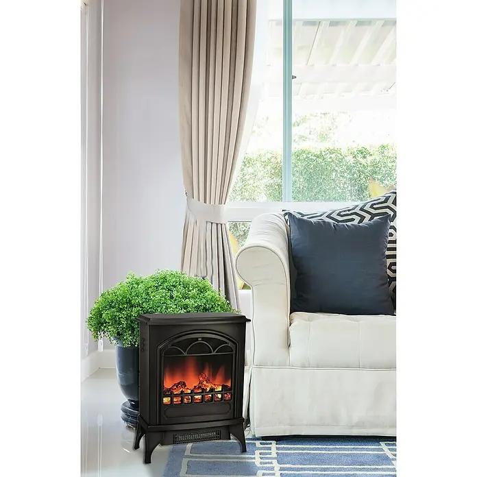 Voltomat HEATING Chimenea eléctrica Lisboa - 1.950 W, Negro, 24 x 39 x 56,5 cm - Una chimenea eléctrica con llamas simuladas está al lado de un sofá y una ventana. Aporta calidez y ambiente.
