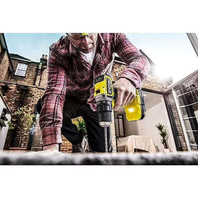 Ryobi ONE+HP Taladro atornillador percutor de batería RPD18C - 18 V, Sin batería, 0 Ah, 50 Nm - Hombre con camisa de cuadros taladra con un taladro inalámbrico Ryobi amarillo y negro.