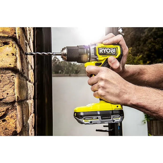 Ryobi ONE+HP Taladro atornillador percutor de batería RPD18C - 18 V, Sin batería, 0 Ah, 50 Nm - Primer plano de un taladro percutor inalámbrico amarillo Ryobi ONE+ HP perforando una pared de ladrillo.