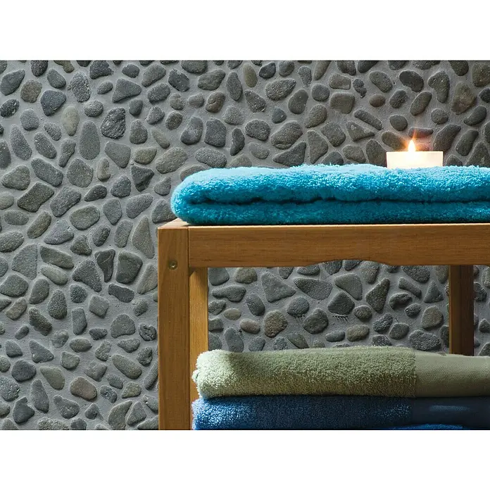 Malla mosaico Rocamar - 30 x 30 cm, Gris/verde - Toallas coloridas están apiladas ordenadamente en un estante de madera, complementadas con una vela encendida y una pared de piedra decorativa.